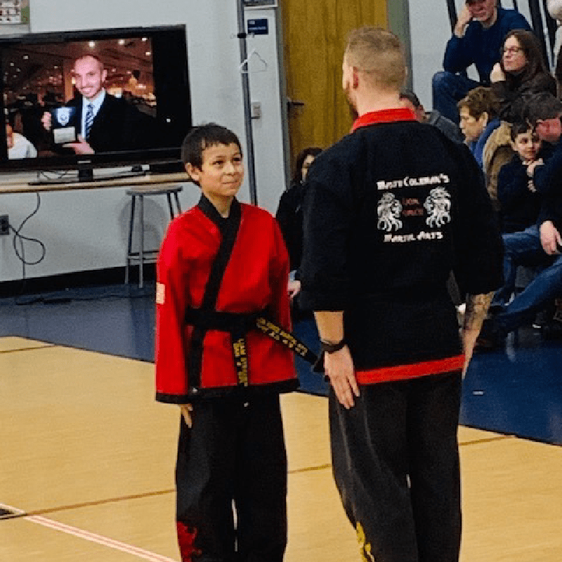 A young boy in a red martial arts uniform standing next to an instructor in a black uniform